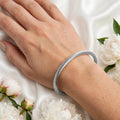 Close-up of hand wearing silver twisted cable bangle with white flowers - Avenzra Twisted Cable Bangle